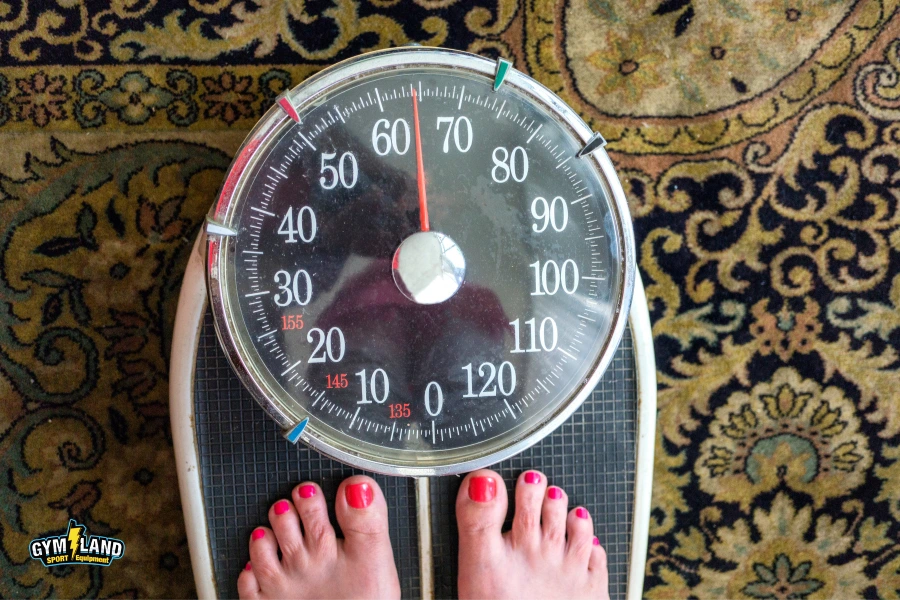 زنی بر روی یک ترازو با پاهای لاک زده که ترازو، وزن 64 کیلوگرم را نشان می دهد.